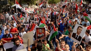 Syrians citizens waving national flags and holding photos of Syrian President Bashar Assad during a pro-government rally in Aleppo province, Syria, April 29, 2014